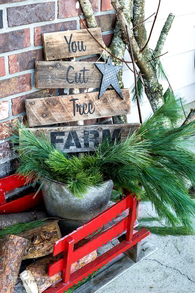 A festive tree farm themed Christmas front porch, infused with branches, a sage green door and a tree farm sign in a wooden sleigh. Made with Funky Junk's Old Sign Stencils and Fusion Mineral Paint \ tour at funkyjunkinteriors.net