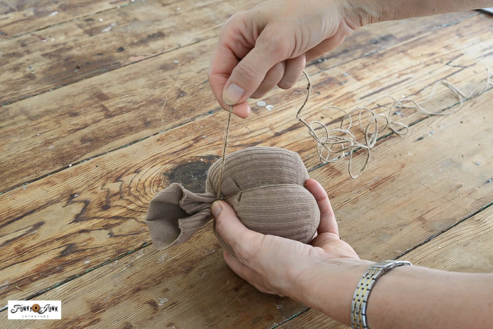 wrapping twine around a stuffed sock to create a fabric pumpkin