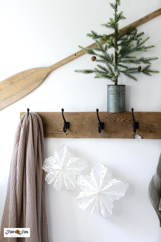 paper snowflakes made from doilies, hanging from a row of black and wood hooks for a wonderful winter decor display
