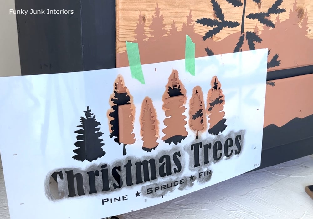 stenciling different sized forest trees on a dresser to create a realistic painted landscape